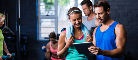A man and woman looking at fitness software on an Ipad in a gym
